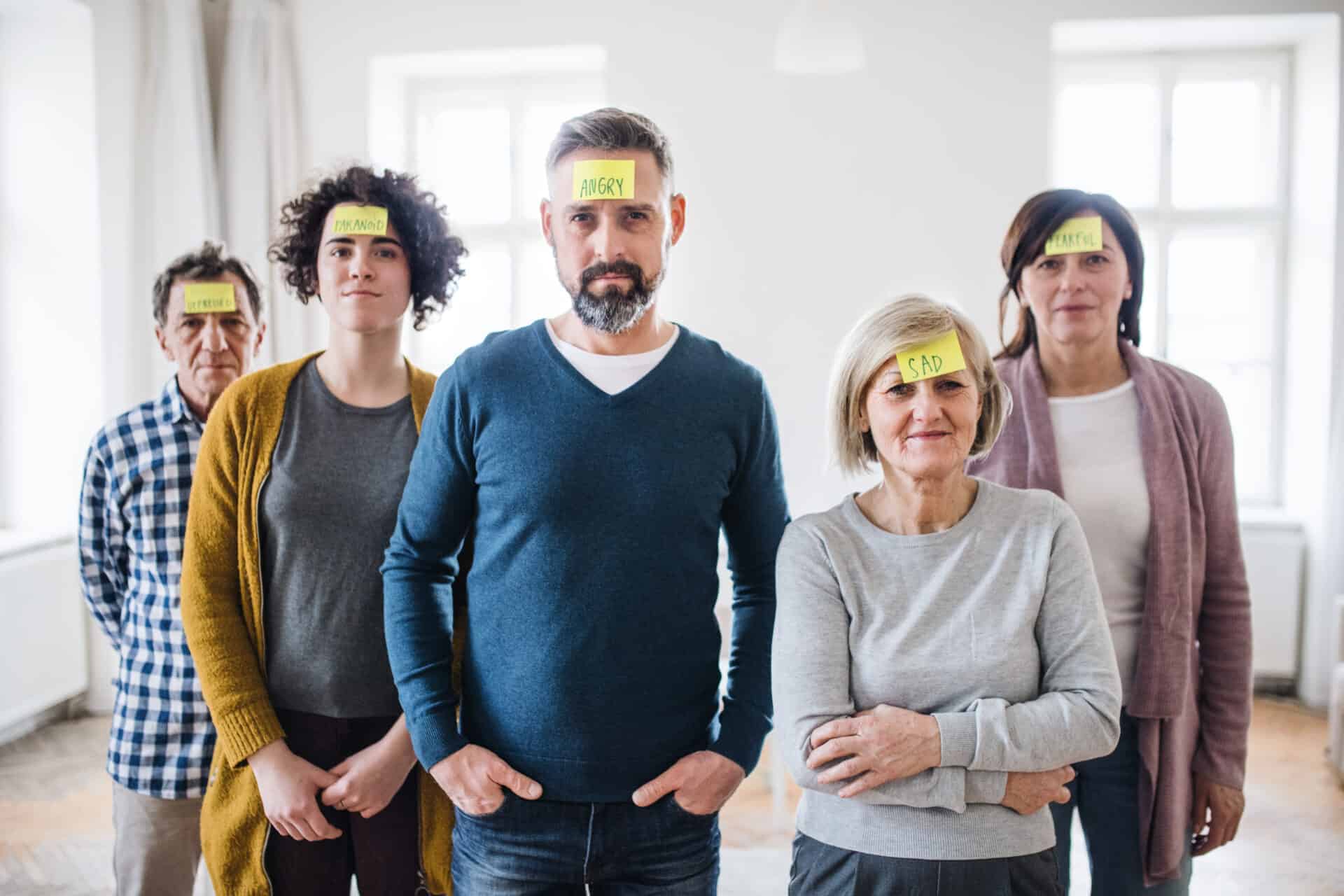 Young and old people standing with negative emotions adhesive notes during group therapy.