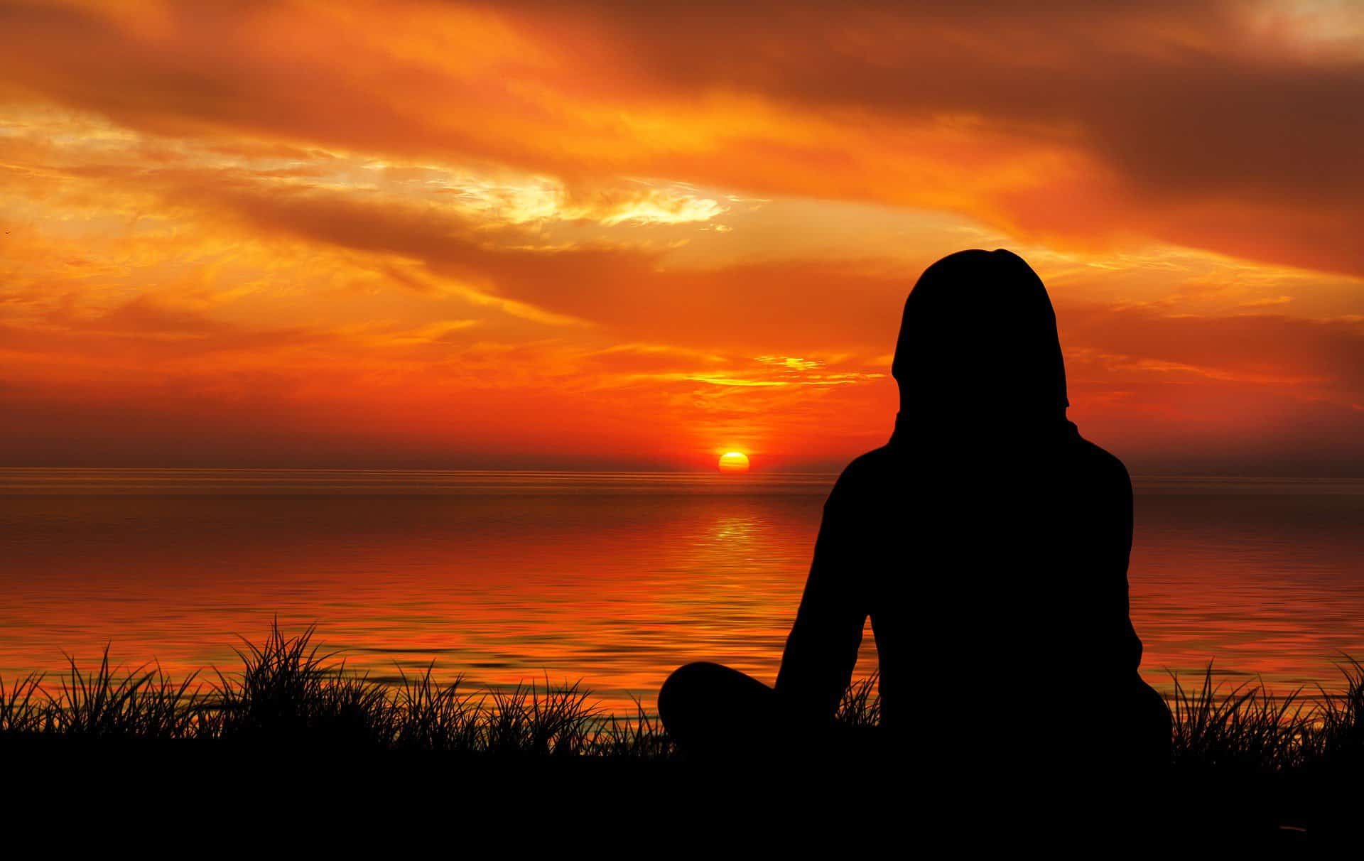 A silhouette of a woman sitting on the beach watching the sunset.